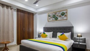 A bedroom with a large bed, a wardrobe, a bedside table, and a decorative wall piece. - Hotel Fortune Home (Noida)