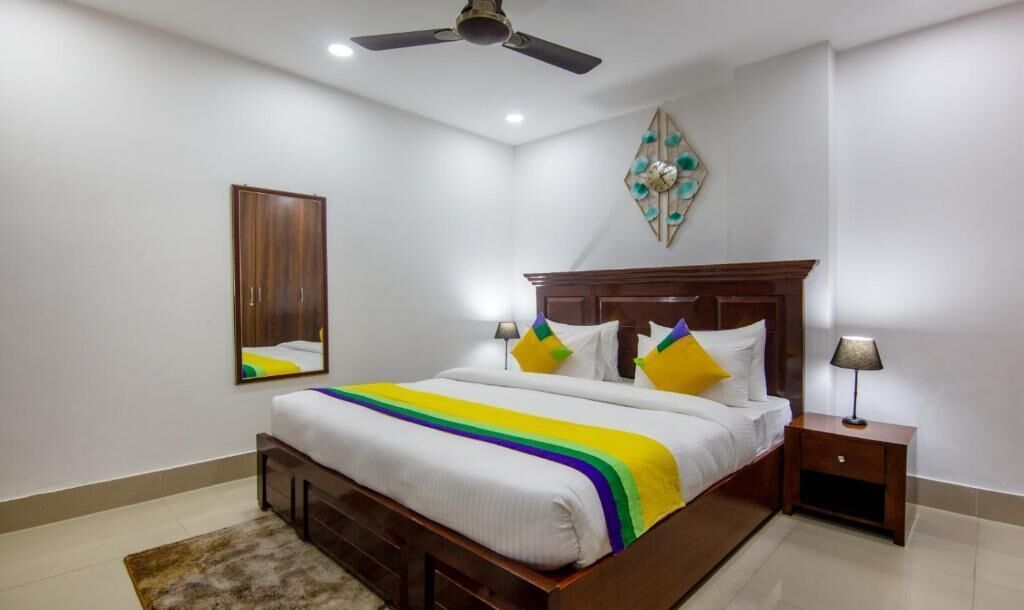 A bedroom with a bed, nightstands, a ceiling fan, a mirror, and a decorative wall piece.