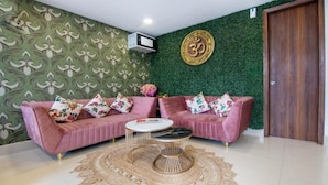 A room with a green patterned wallpaper, a pink sofa with floral cushions, a round coffee table, and a wall-mounted air conditioner. - Hotel Fortune Home (Noida)