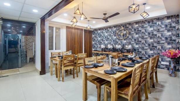 A dining area with wooden tables and chairs, pendant lights, and a patterned wall. - Hotel Fortune Home (Noida)