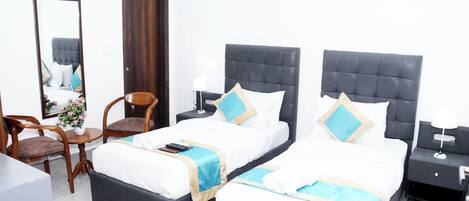 A hotel room with two beds, a desk, a chair, a mirror, and a wardrobe.