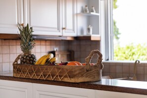 Un panier en bois rempli de fruits est posé sur un plan de travail dans la cuisine, avec une fenêtre en arrière-plan.