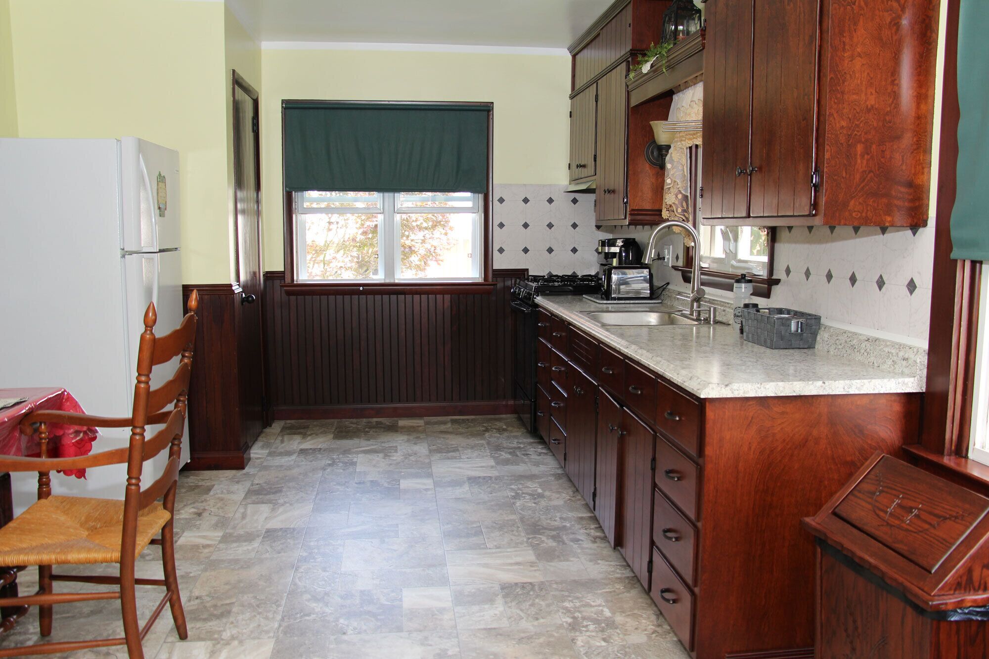 Una cocina con armarios de madera, estufa, fregadero y una silla.