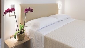 A neatly made bed with white linens, a beige headboard, and a small wooden nightstand with a potted orchid. - Hotel Dalì near Pompei - Naples (Scafati)