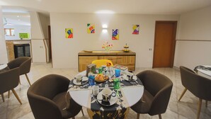 A dining area with a table set for four, surrounded by brown chairs. A wooden cabinet with a yellow chair is in the background. - Hotel Dalì near Pompei - Naples (Scafati)