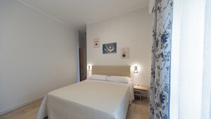 A neatly made bed in a room with a plain wall and a small bedside table. - Hotel Dalì near Pompei - Naples (Scafati)