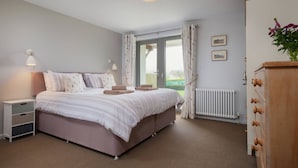 A bedroom with a large bed, bedside lamps, a dresser, and a view of the outdoors.