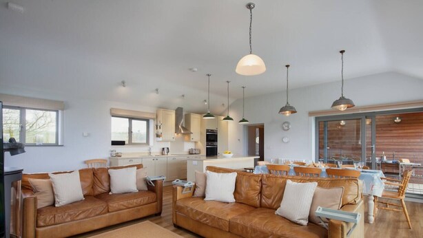 Eine moderne Küche mit Pendelleuchten, ein Essbereich mit Holzmöbeln und ein Wohnzimmer mit Ledersofas.