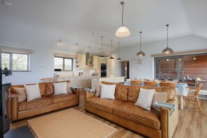 Eine moderne Küche mit Pendelleuchten, ein Essbereich mit Holzmöbeln und ein Wohnzimmer mit Ledersofas.