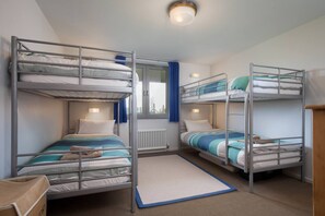 Ein Schlafsaalzimmer mit Etagenbetten, einem Fenster mit Vorhängen, einem Heizkörper und einem kleinen Teppich.