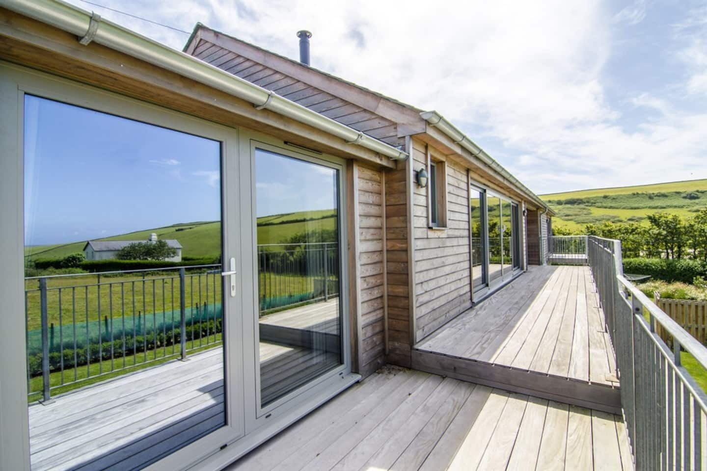 A wooden deck with large sliding glass doors leading to a scenic view of a green landscape.