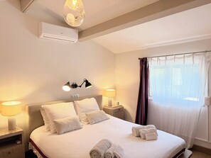 A hotel room with a bed, two bedside lamps, a wall-mounted air conditioner, and a window with curtains. - Peps Pink Flamingos, 2 bedrooms, pool, near downtown (Saint-Rémy-de-Provence)