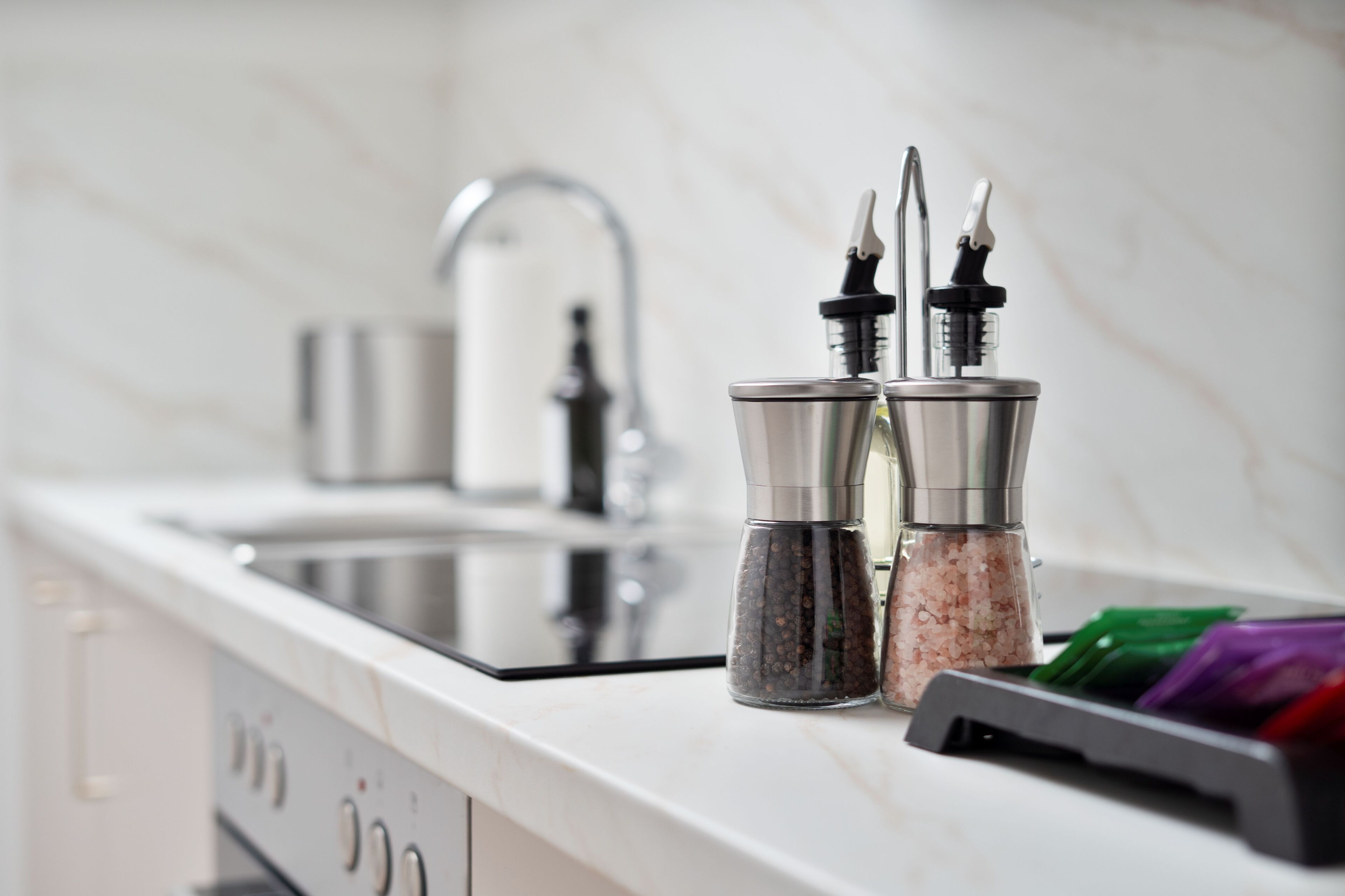 Una encimera de cocina con un lavabo, dos saleros y pimenteros, y un escurreplatos con utensilios.