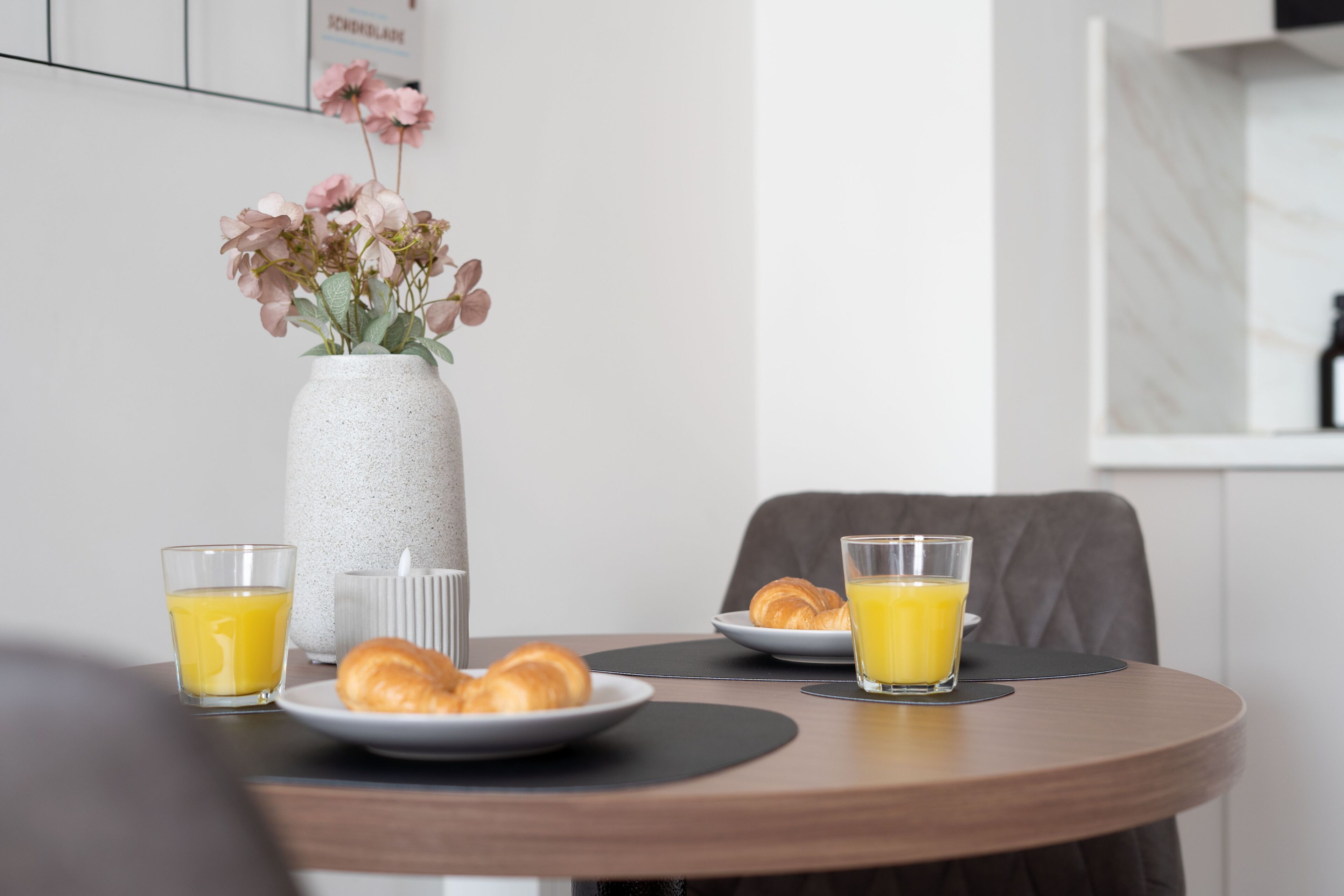 A breakfast table with croissants, orange juice, and a vase with flowers.