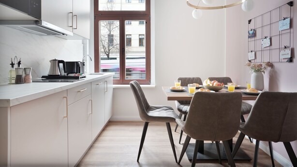 Eine moderne Küche mit weißen Schränken, einer eingebauten Mikrowelle und einem Essbereich mit Tisch für zwei Personen.