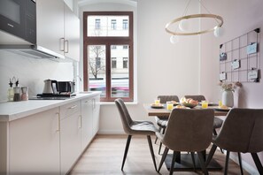 A modern kitchen with white cabinets, a built-in microwave, and a dining area with a table set for two. - Premium apartments I home2share (Halle (Saale))