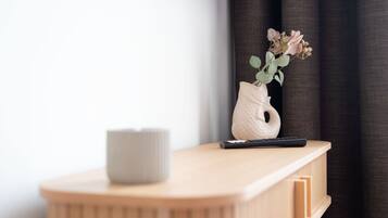 Une table de chevet en bois, ornée d’un vase de fleurs, d’une télécommande et d’une bougie.