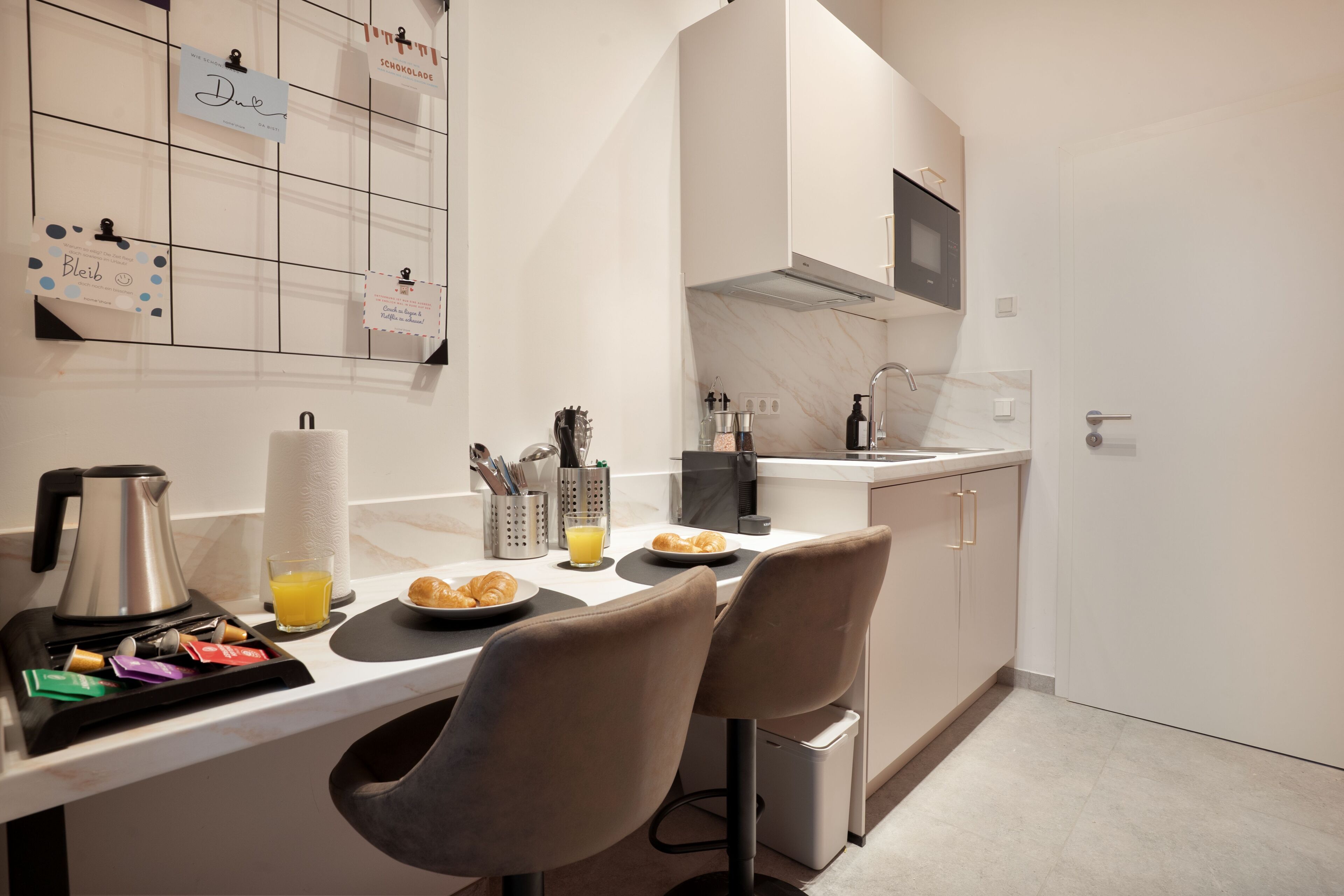 Eine moderne Küche mit Marmorarbeitsplatte, zwei Barhocker, einer Kaffeemaschine, einem Glas Orangensaft und einem Frühstücksteller mit Croissants.