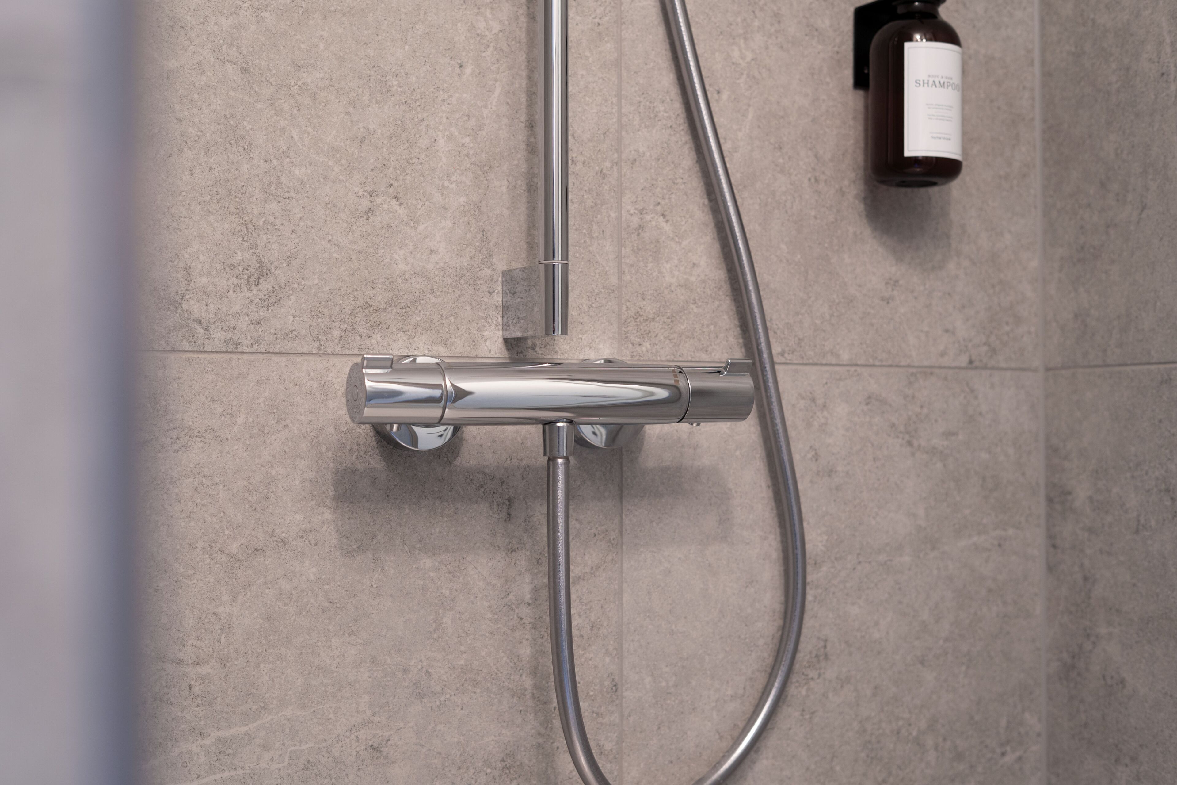 Una ducha moderna con cabezal de ducha manual y grifo empotrado en una pared de azulejos.