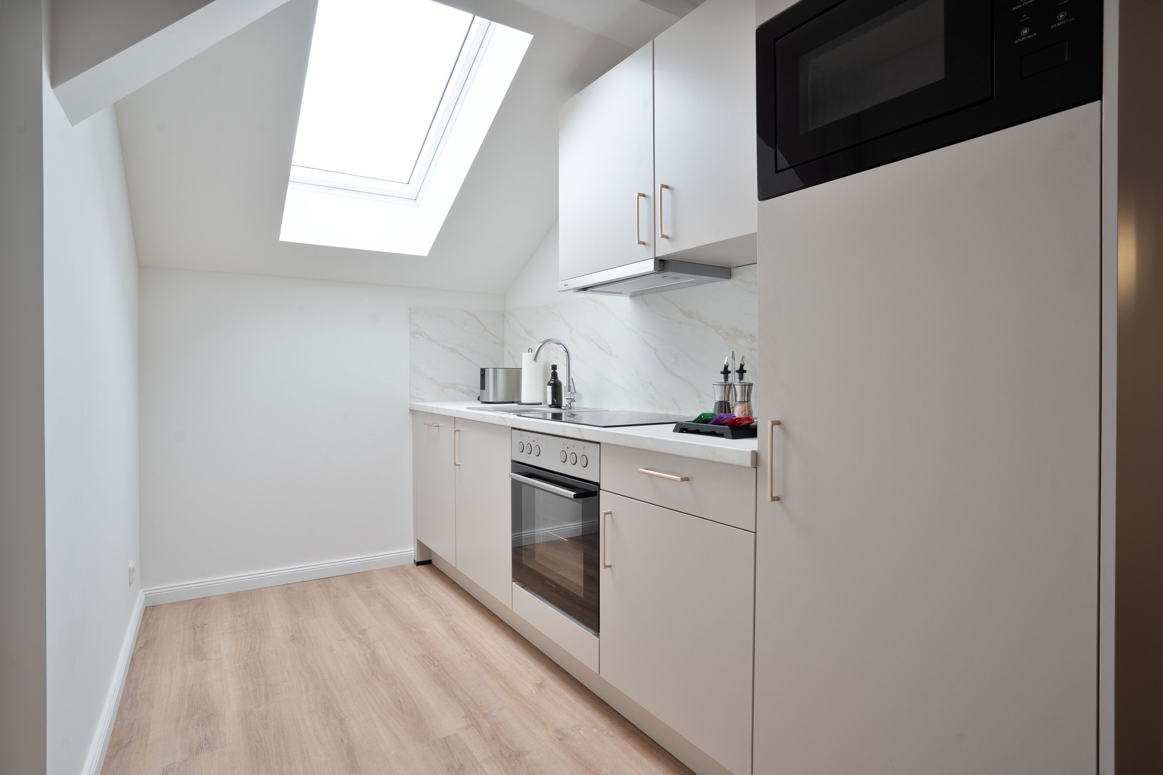 Een moderne keuken met witte kasten, een ingebouwde oven en een magnetron.