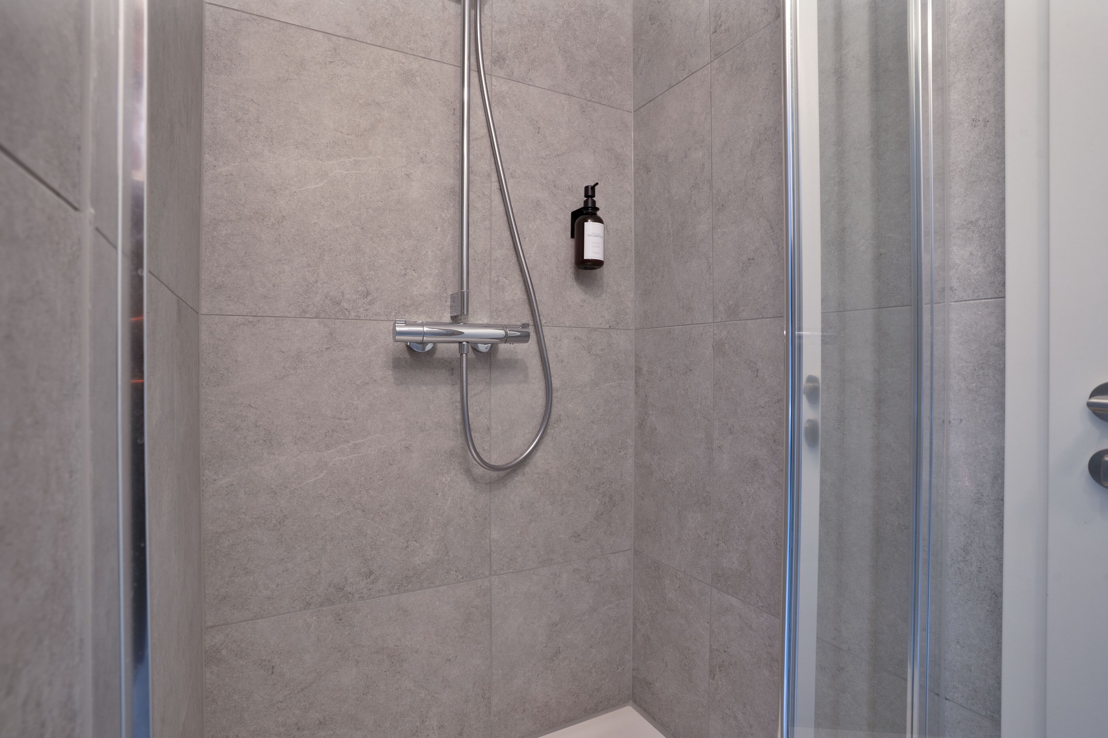 A modern shower with a handheld showerhead and a wall-mounted soap dispenser.