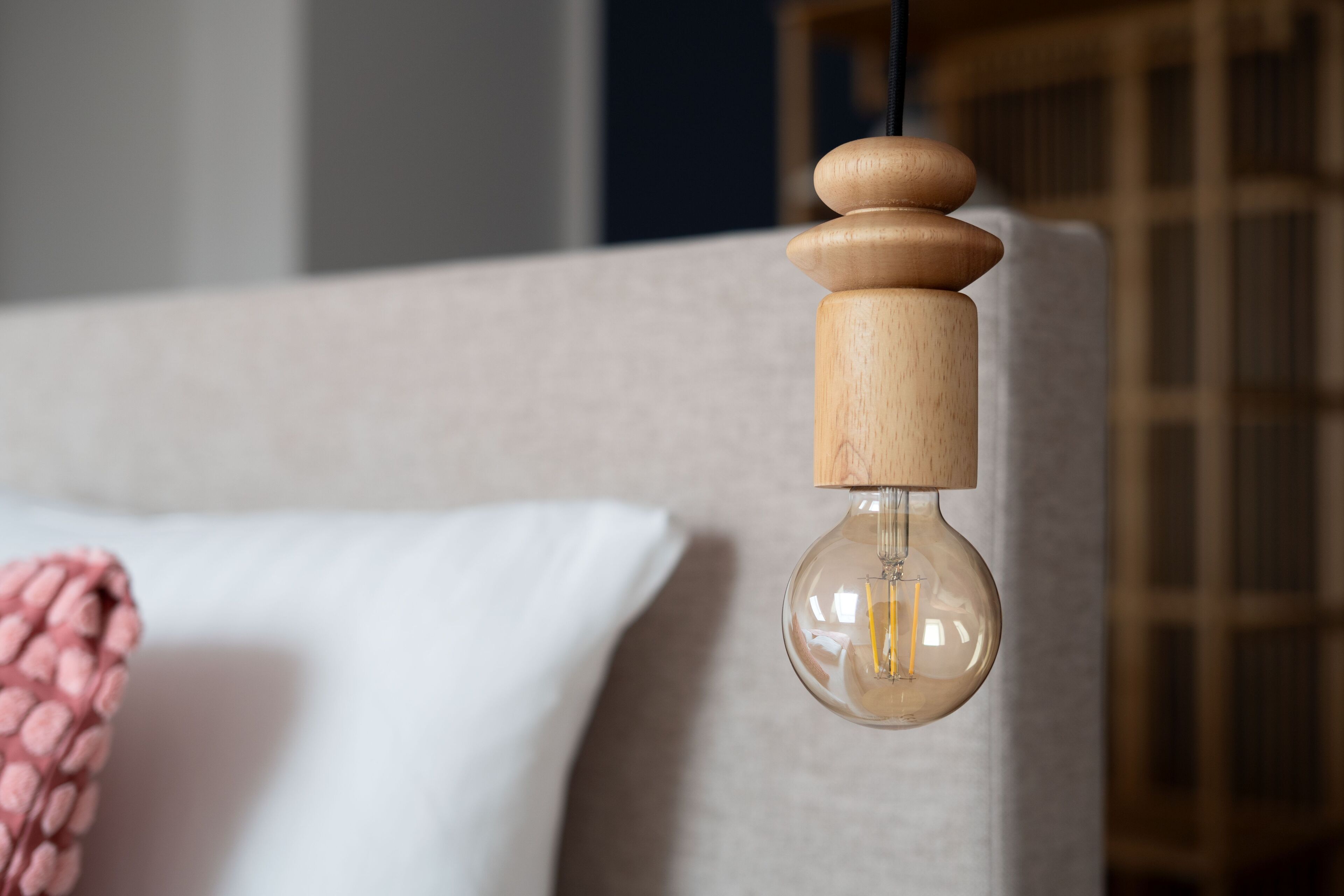 A hanging light fixture with a wooden base and a clear glass bulb, mounted on a wall.