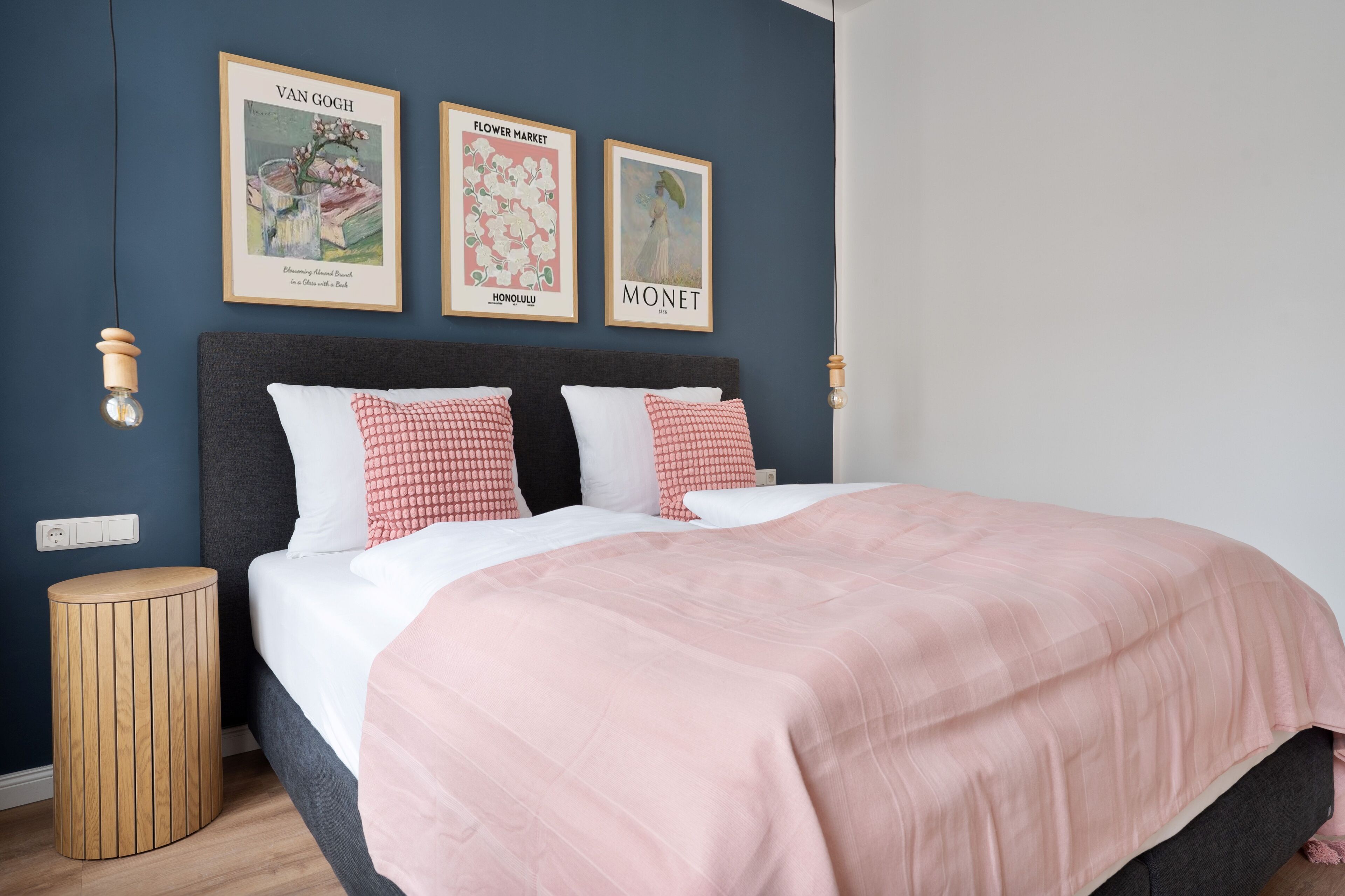 Ein Schlafzimmer mit dunkel gebeiztem Kopfteil, einer rosa Bettdecke und zwei gerahmten Postern an der Wand.