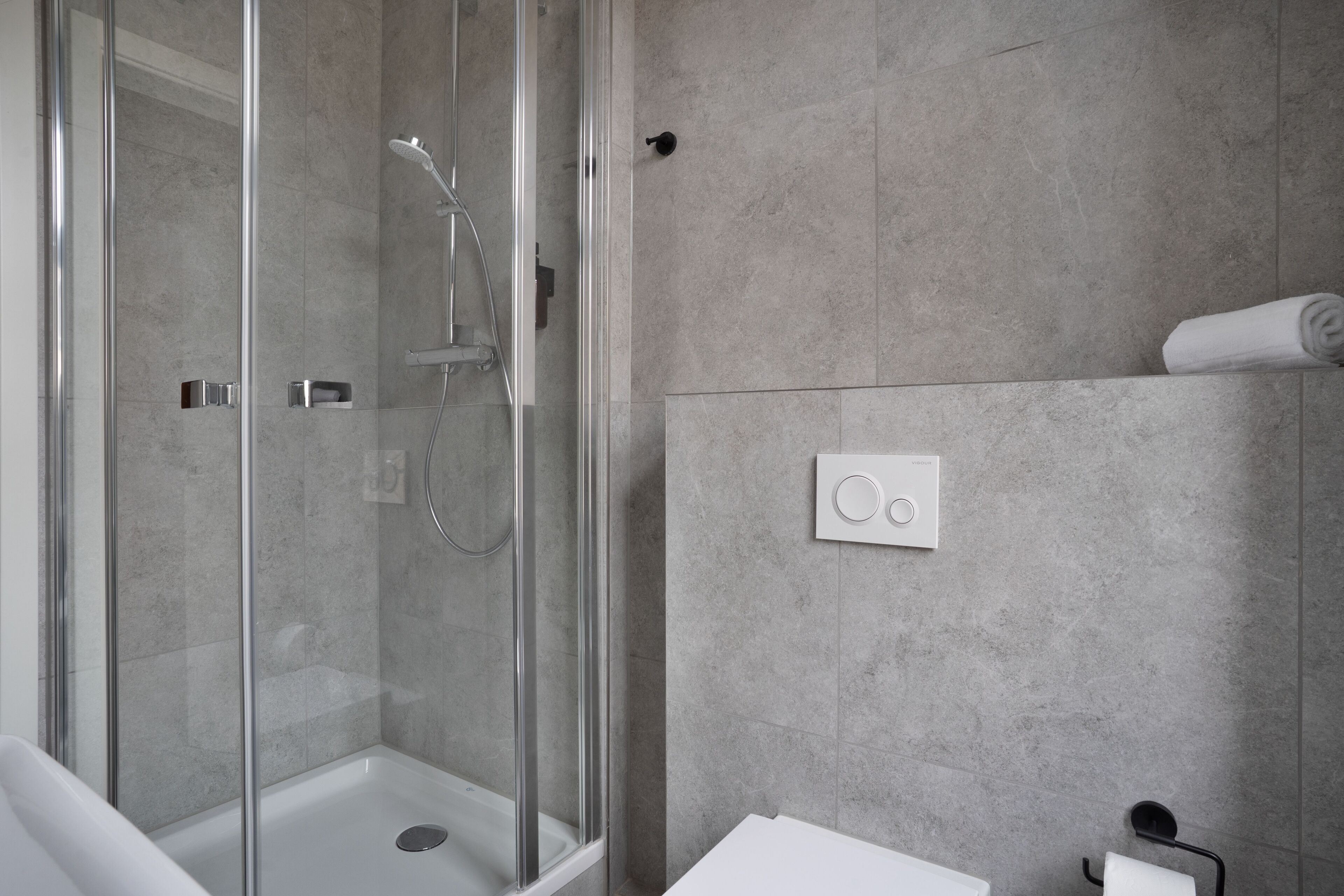 A modern bathroom with a glass-enclosed shower, a white sink, and a towel rack.