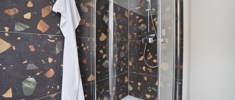 A shower with a glass door, a white towel hanging on the wall, and terrazzo tile flooring.