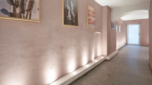 Ein Flur mit einer Wand in Rosa, strukturierter Oberfläche, gerahmten Kunstwerken und einem gefliesten Boden.