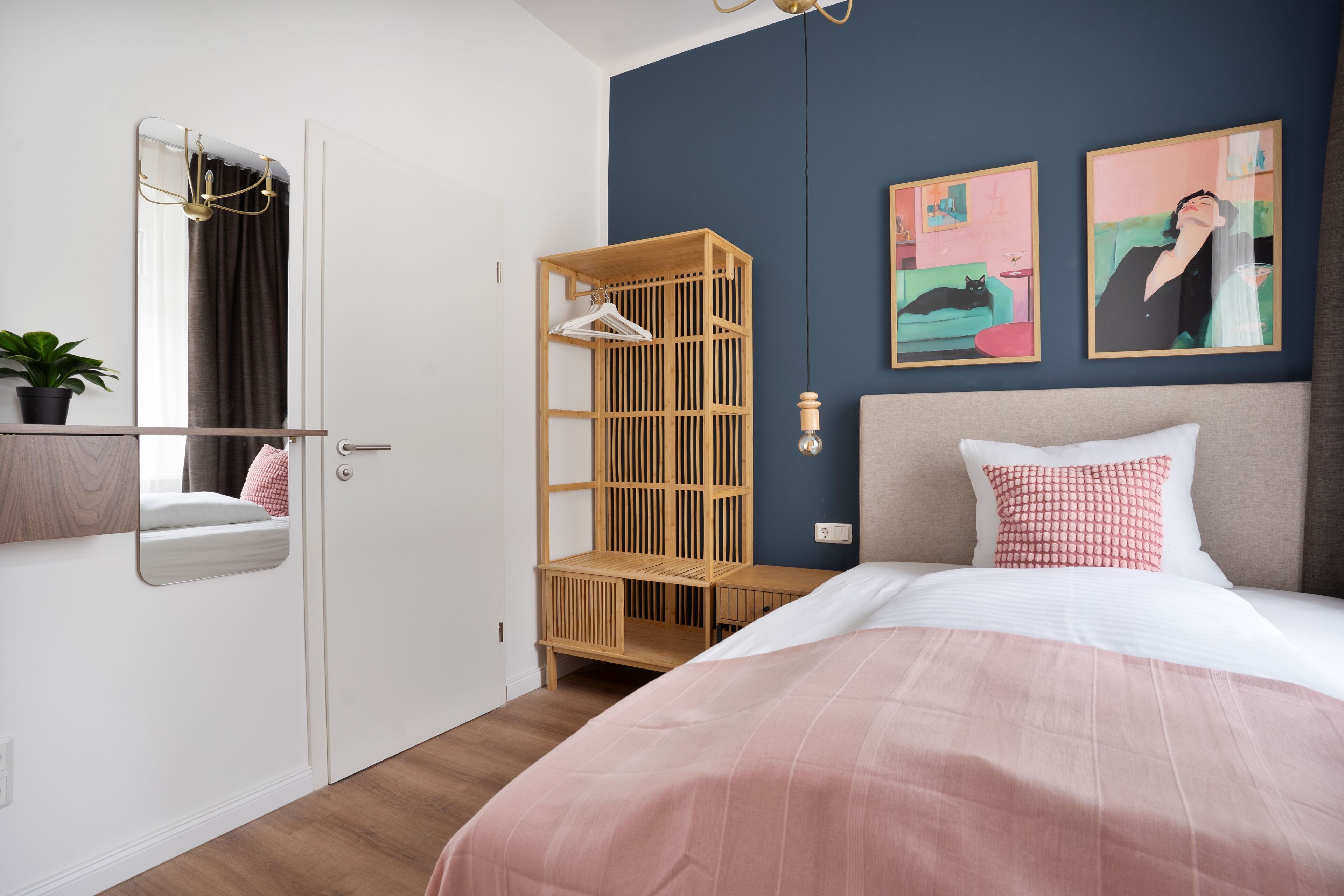 A bedroom with a bed, a wardrobe, a mirror, and two paintings on the wall.