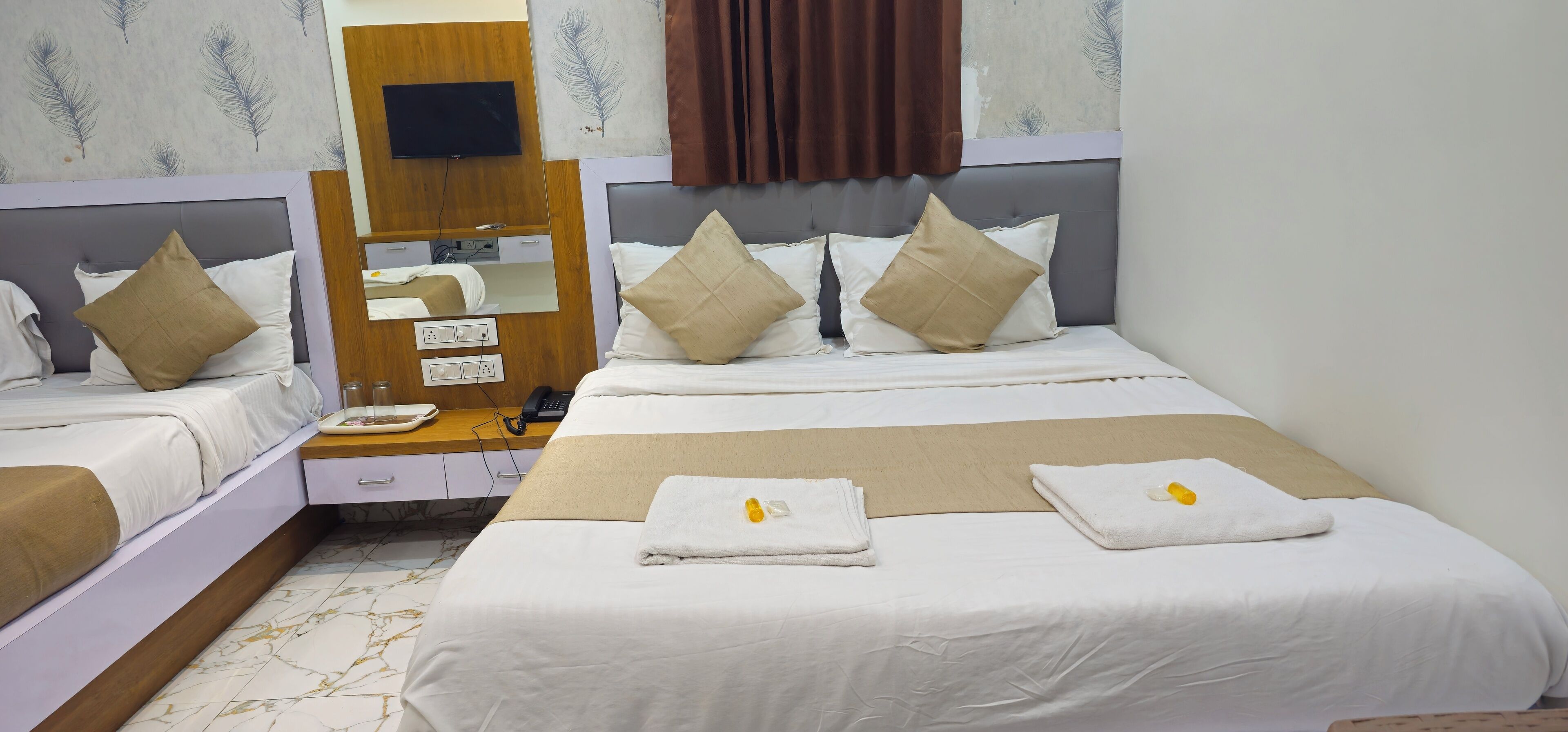 A hotel room with two beds, a desk with a computer, a flat-screen TV, and a large window with curtains.