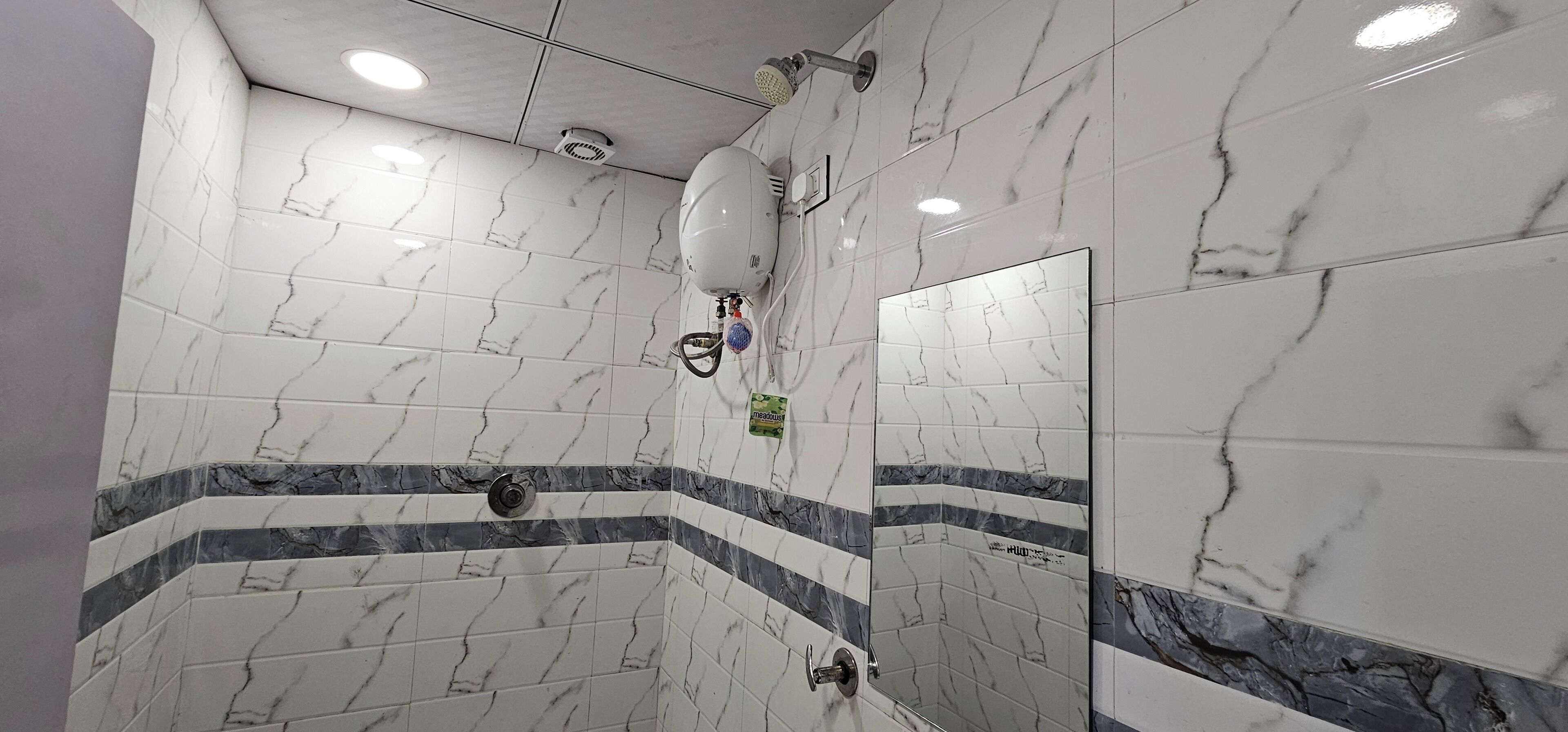 A bathroom with white marble tiles, a shower area, and a mirror.