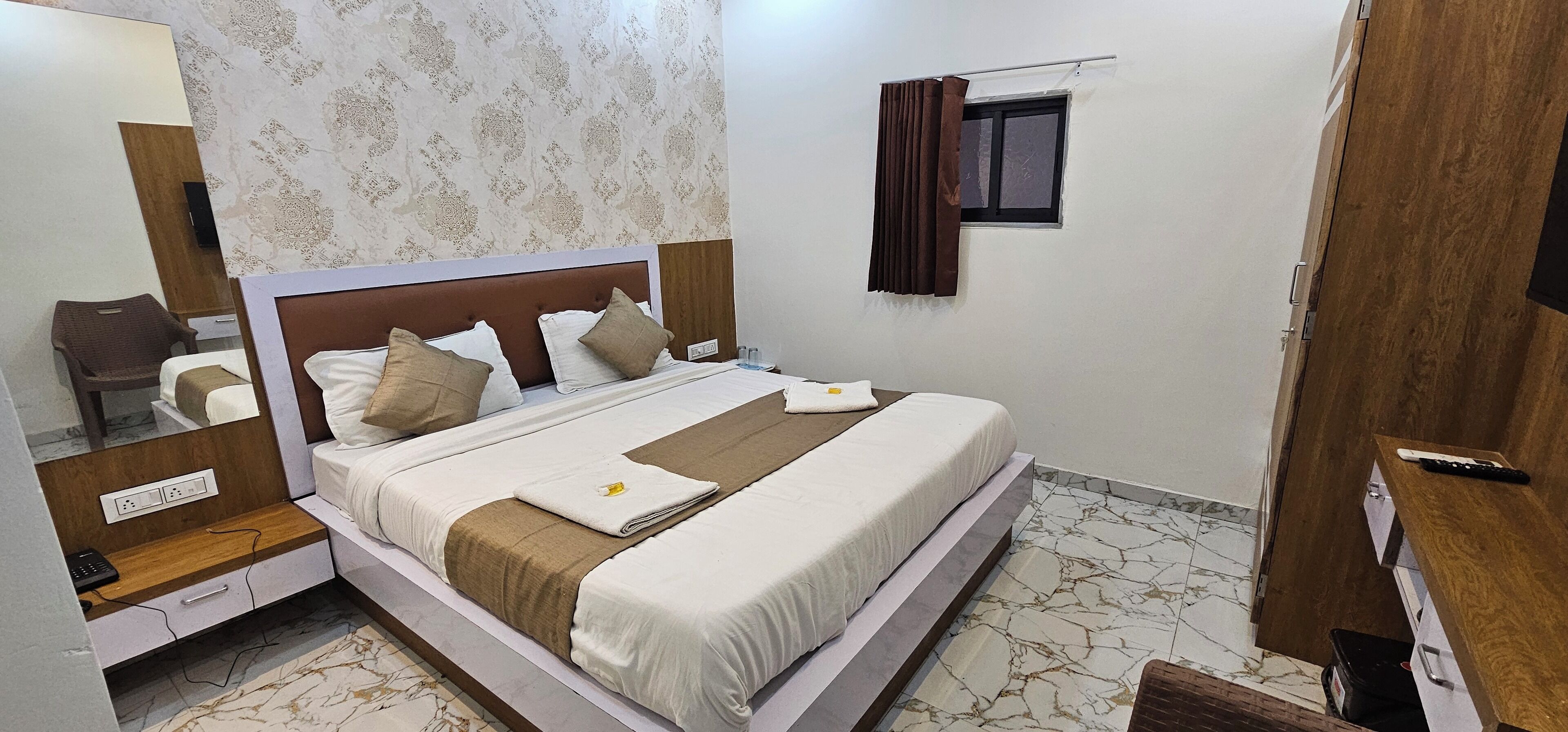 A neatly made bed with a headboard, a bedside table with a phone, and a small window with curtains.
