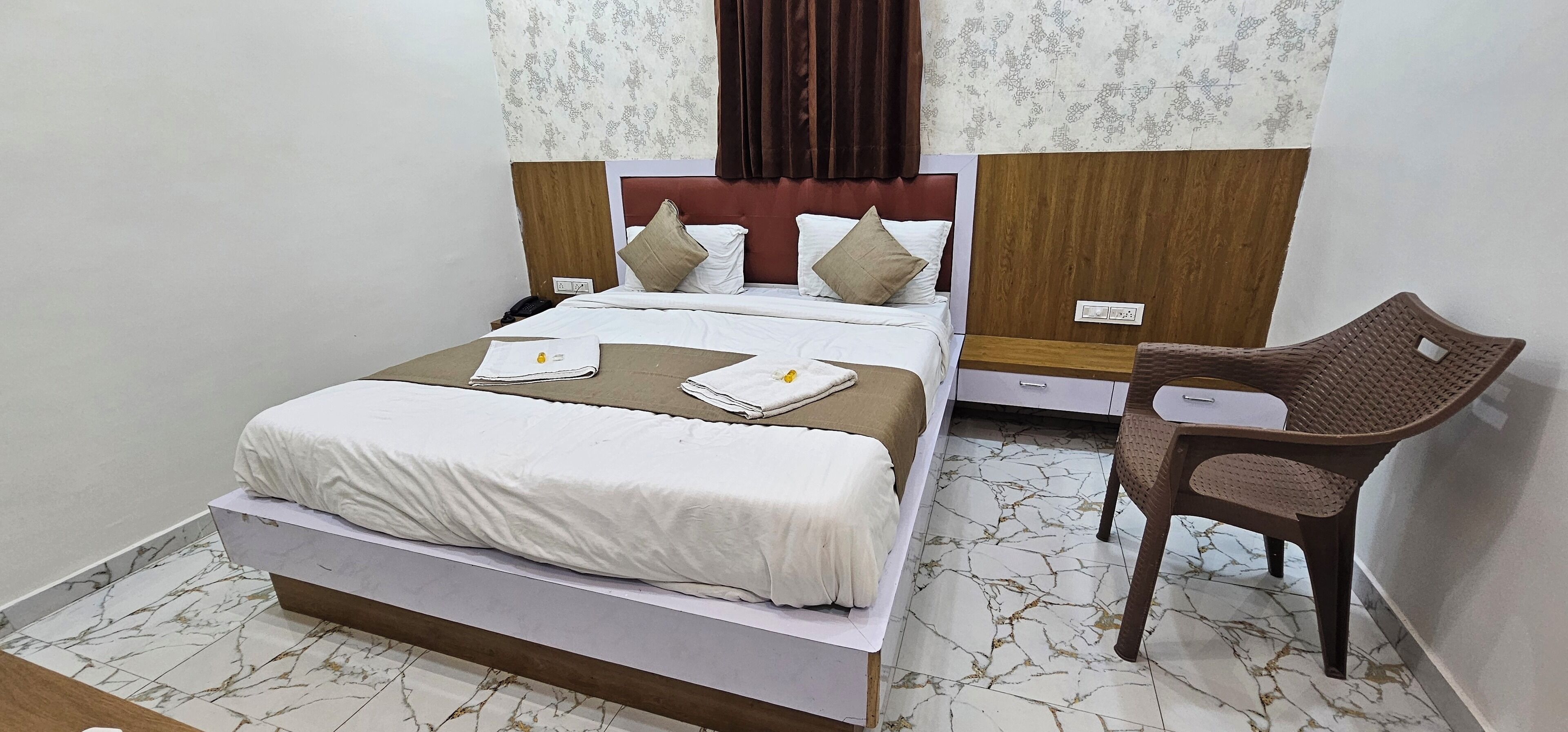 A neatly made bed with a white and brown bedspread, a wooden headboard, and a brown chair beside it.
