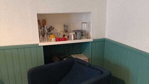 A corner room with a dark blue armchair, a white shelf with kitchen items, and green paneled walls. - Studio historic center Périgueux (Périgueux)