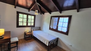 Una habitación pequeña y acogedora con una cama individual, un escritorio con lámpara y dos ventanas con cortinas.