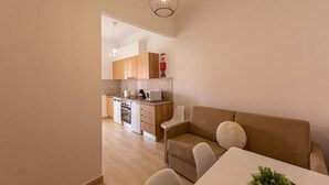 Ein modernes Wohnzimmer mit Sofa, Esstisch und einer Küche im Hintergrund.