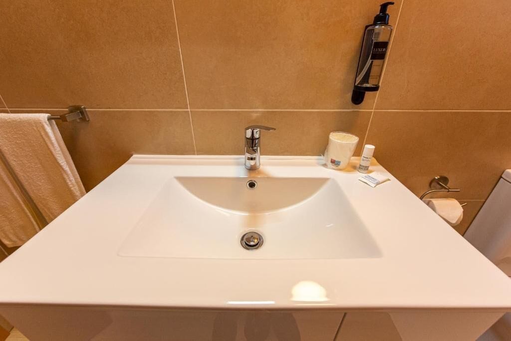 Un baño con un lavamanos blanco, un perchero para toallas, un dispensador de jabón y un porta papel higiénico.