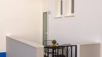 A small, enclosed balcony area with a table and chairs, a potted plant, and a door leading to an interior space.