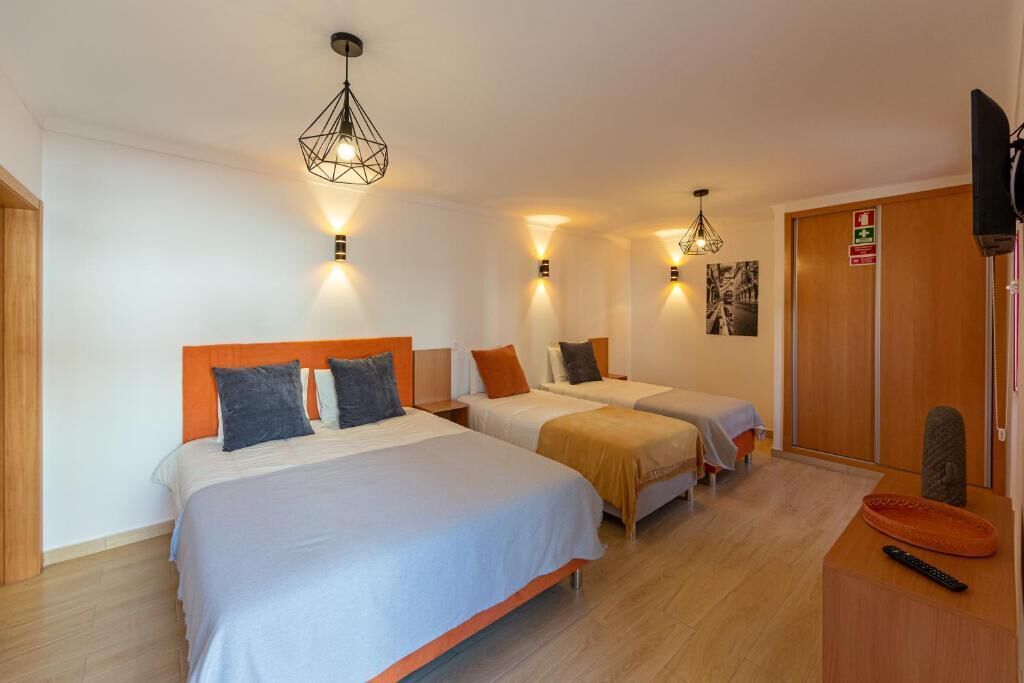 A hotel room with two beds, a wooden wardrobe, a TV, and a small table with a remote control.