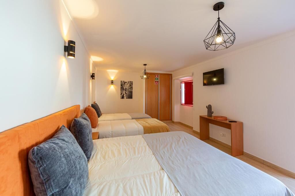 Habitación de hotel con dos camas, cabecero de madera, escritorio pequeño y televisión en la pared.