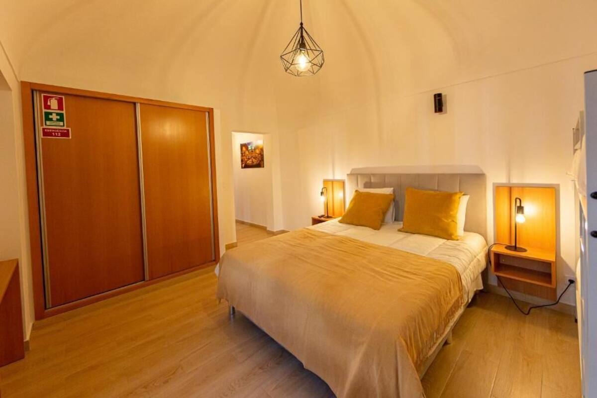 Habitación de hotel con una cama grande, armario de madera, lámparas de noche y una lámpara en el techo.