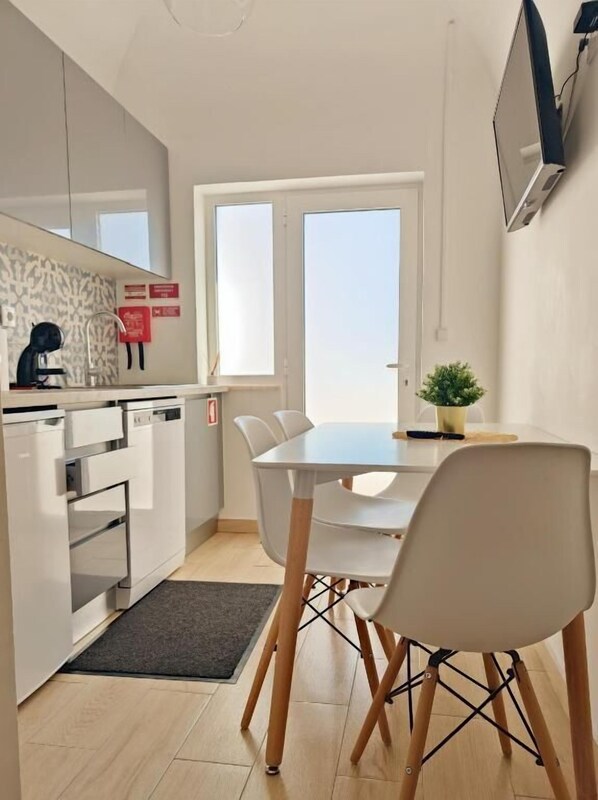Une cuisine moderne avec des appareils électroménagers blancs, une table à manger avec des chaises, une petite plante en pot et une fenêtre donnant sur un beau paysage.