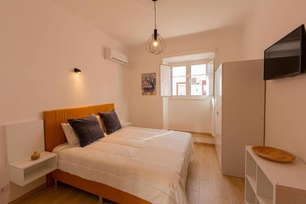 Un dormitorio con una cama doble, una mesita de noche, un televisor montado en la pared y una ventana con puerta abierta.
