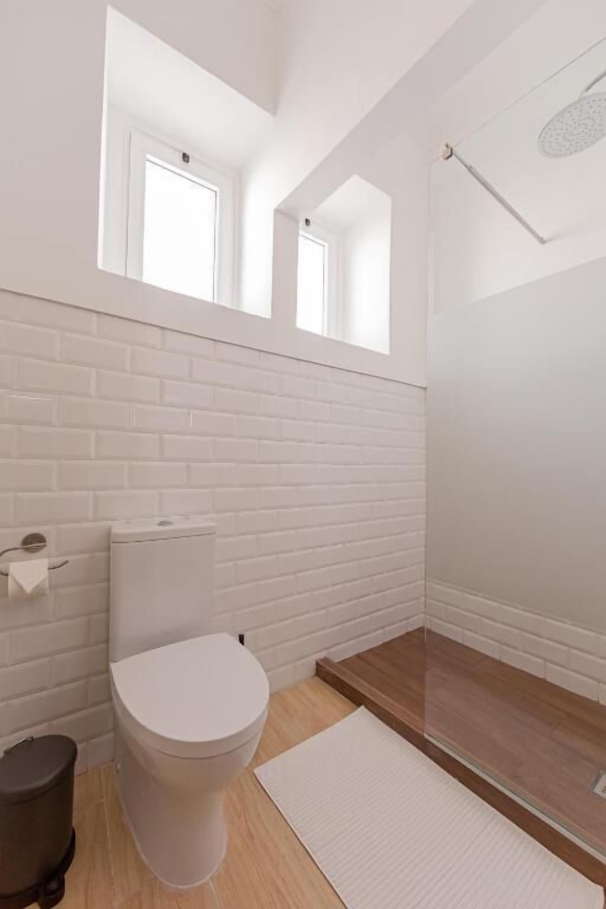 A modern bathroom with a white toilet, a trash bin, and a shower area.