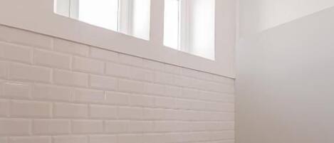 A modern bathroom with a white toilet, a trash bin, and a shower area.