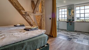 Ein Schlafzimmer mit einem großen Bett, Holzbalken, einem Badezimmer mit Fenster und einer Aussicht.