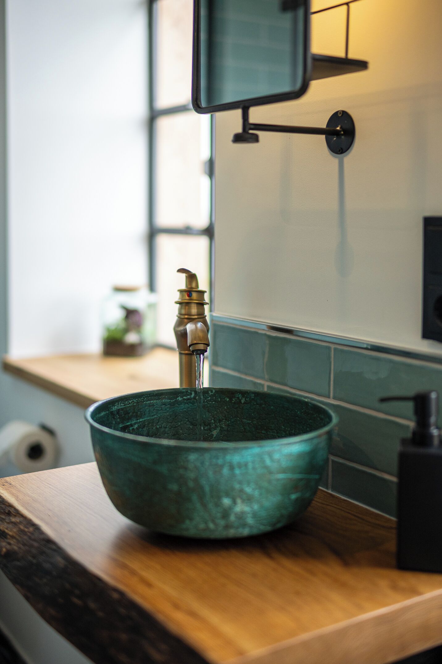 A kitchen sink with a brass faucet, a wooden countertop, and a glass bowl.