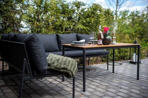 Un canapé noir avec un plaid vert, une table en bois sur laquelle se trouvent une bouteille, un verre et un vase avec une fleur rouge.